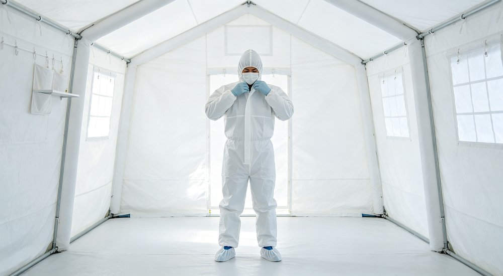 PPE donning area inside inflatable isolation tent anteroom, worker putting on protective gear red and white inflatable emergency shelter for disaster relief operations